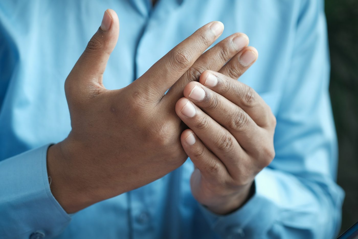 Close-up of a person in a blue shirt rubbing a stiff, aching hand and fingers.