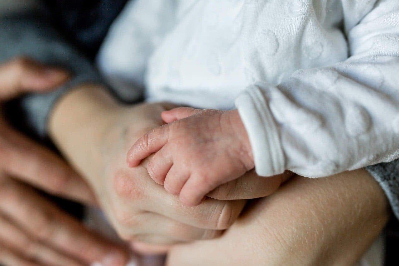 A newborn's hand holding a parent's hand
